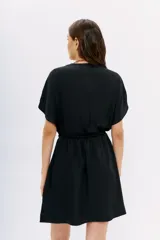 Vestido corto de color negro con escote cruzado, mangas cortas y cintura elastizada. Presenta un diseño de calce relajado y fluido.