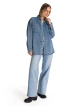 Camisa oversize de denim azul de la marca Cat, de manga larga con puños abotonados, cuello camisero y cierre frontal de botones. Presenta doble bolsillo en el pecho con etiqueta de la marca y dobladillo tipo cola de camisa.