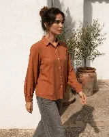 Camisa de color terracota con cuello camisero, cierre frontal de botones y mangas largas con puños elásticos.
