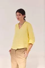 Blusa de lino color amarillo, con escote en V, mangas largas amplias con puños vueltos y ruedo curvo.