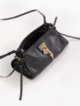 Bandolera de cuero vacuno color negro con efecto brillante, herraje metálico tipo candado y dijes de llave colgantes en tono dorado. Cuenta con correa fina ajustable y tiras laterales decorativas.