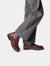Botas de agua de caña baja color bordó, con elásticos laterales a rayas en tonos burdeos, beige y marrón. Cuenta con suela dentada negra, costuras blancas decorativas en el borde y presilla trasera para facilitar el calce.