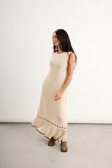 Vestido largo de punto color beige con detalles marrones en cuello, sisas y dobladillo, sin mangas y con diseño de volados en la parte inferior.