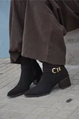 Bota corta de cuero color marrón, con taco cuadrado de madera y punta fina. Presenta una tira decorativa con hebilla metálica dorada alrededor del tobillo.