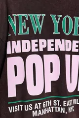 Camiseta de manga larga color marrón oscuro con efecto lavado. Presenta un cuello redondo y un estampado en el pecho con el texto "NEW YORK" en verde y "POP UP" en rosado.