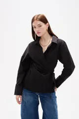 Camisa blanca de algodón con diseño cruzado y anudado lateral, cuello camisero y mangas largas con puños.