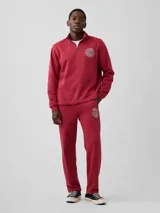Pantalón deportivo de ajuste holgado color rojo, con bolsillos laterales y elástico en la cintura. Presenta un logo circular estampado en la pierna izquierda.