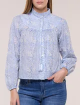 Blusa celeste de algodón con estampado floral, cuello mao fruncido con volado y cordel frontal con borlas. Tiene mangas largas abullonadas con puños elásticos y abotonadura frontal.