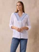 Blusa blanca de poliéster y rayón con escote en V bordado y mangas tres cuartos regulables con presilla y botón.