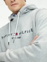Buzo hoodie gris de Tommy Hilfiger con logo bordado en el pecho, cordones blancos y bolsillo tipo canguro.