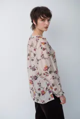 Camisa de corte holgado con estampado floral en tonos rojizos y verdes sobre base beige. Presenta cuello mao con escote en V, cierre frontal parcial con botones y mangas largas con puños ajustados.