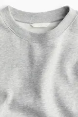 Buzo de tejido de punto color gris melange, con cuello redondo, hombros caídos y puños y bajo acanalados.