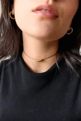 Gargantilla con tiento de hilo encerado color borgoña y dije tubular de acero quirúrgico dorado.