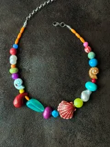 Collar corto con cuentas de cerámica, cristales checos y acrílico de diferentes colores y formas. Incluye una concha roja como dije central.