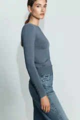 Jersey de punto liso color negro, con cuello redondo y manga larga. Presenta una hilera de cuatro botones dorados decorativos en el puño de cada manga.