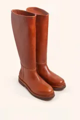 Bota de caña alta confeccionada en cuero vacuno suave, con diseño minimalista y suela de goma robusta. Presenta costuras visibles en la zona del empeine y un taco bajo cuadrado.