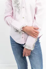 Camisa rosa pálido de manga larga con cuello camisero y volados grises en el frente y los puños.