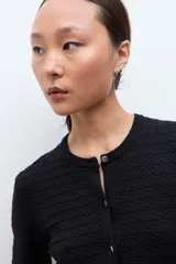 Cardigan negro de manga larga con cuello redondo y cierre frontal de botones. Presenta un tejido con patrones estructurados y un borde festoneado en el dobladillo.