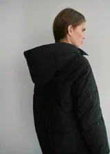 Campera puffer negra con capucha, cuello alto y cierre frontal de cremallera doble. Diseño acolchado de manga larga con acabado repelente al agua.