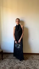 Vestido largo negro de corte halter con escote buche y espalda descubierta, de silueta relajada en forma de A. Cuenta con textura tridimensional de flores y relieves orgánicos.