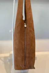 Bolso tipo hobo grande confeccionado en cuero vacuno color marrón, con costura central vertical y placa metálica con el logo de la marca Pecarí.