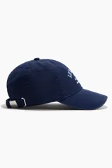Gorra de sarga de algodón en color azul marino con efecto lavado, visera curva y diseño bordado en el frente con el texto 'Le Marais Paris Est. 1947 Maison Éternité'. Cuenta con botón superior y trabilla ajustable con cierre de metal en la parte trasera.