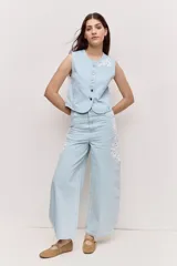 Chaleco de denim claro con escote redondo, cierre frontal de botones y detalles bordados.