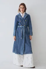 Trench largo de denim azul, con diseño de doble botonadura, solapas clásicas y mangas largas con puños ajustables. Presenta un corte recto y estructurado.