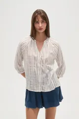 Camisa de algodón con diseño de rayas verticales y detalles bordados. Presenta cuello en V, cierre frontal con botones y mangas tres cuartos con terminación elástica.