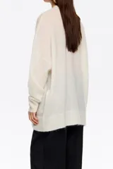 Cardigan largo de corte oversize, color blanco, con escote en pico, cierre frontal de botones y bolsillos de plastrón. Presenta mangas largas con puños acanalados.