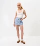 Short pollera de sarga en color celeste claro, con diseño de cinco bolsillos, trabillas para cinturón y cierre frontal con botón metálico. Presenta un corte recto y ajustado con acabado deslavado.