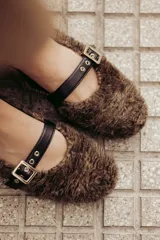 Bailarinas marrones con exterior de pelo sintético y tira de cuero con hebilla metálica.