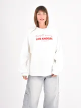 Buzo negro de corte holgado con cuello redondo y mangas largas con puños elásticos. Presenta un estampado frontal con la frase 'Shine Bright' en tipografía cursiva y texto complementario en blanco.