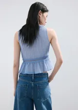 Top celeste sin mangas, de cuello en V y cierre frontal con cordones ajustables. Presenta detalles de puntilla en el escote y en la cintura, con diseño peplum en el bajo.