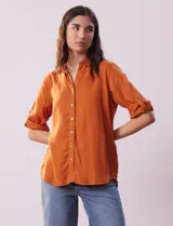 Camisa color beige de tencel, marca Hester & Orchand, con cuello con solapa, escote en V, abertura central con botones y bolsillos delanteros. Las mangas son largas y regulables con presilla y botón.