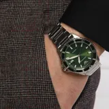 Reloj de pulsera Emporio Armani con caja de 42 mm y malla de acero inoxidable plateado. Presenta una esfera verde con acabado sunray, manecillas e índices luminiscentes, ventana de fecha a las 3 y bisel giratorio bicolor.