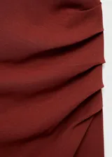 Vestido midi de fiesta color terracota, con cuello barco y diseño sin mangas. Presenta detalles fruncidos en la cintura y un detalle de nudo en el hombro, con un corte entallado y cierre posterior.
