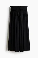 Pollera maxi negra de corte holgado, confeccionada con cintura elástica fruncida y cordón ajustable con borlas colgantes.