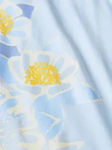 Remera de corte regular confeccionada en algodón, color celeste, con cuello redondo y mangas cortas. Presenta un diseño estampado de flores en el lateral inferior izquierdo y el logo de la marca bordado en la manga.