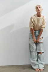 Jeans de tiro medio con corte baggy y diseño de cinco bolsillos. Presenta roturas localizadas en las piernas y cierre frontal con cremallera y botón metálico.