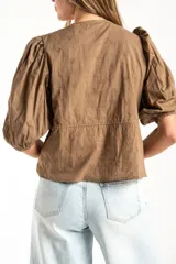 Blusa blanca de algodón con delicado bordado floral, mangas abullonadas de largo 3/4 y cierre frontal con botones y cordón ajustable en la cintura.
