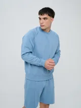 Buzo de felpa bordó, estilo relaxed, con cuello redondo y mangas raglán. Presenta puños y dobladillo acanalados, y una pequeña etiqueta con el logo de Umbro en el lateral inferior.