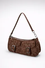 Cartera mini tipo baguette de gamuza color chocolate con estampado animal print sutil. Presenta dos bolsillos frontales con solapa y hebillas metálicas decorativas, cierre superior y asa corta para llevar al hombro con detalle de cadena en un extremo.