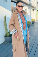 Trench reversible de corte largo, con un lado en color tostado liso y el otro lado con estampado de cuadros. Presenta cuello solapa, cierre frontal de botones, bolsillos laterales y puños con detalle de estampado a cuadros.