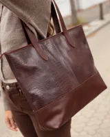 Bolso tipo tote de cuero vacuno color chocolate, con textura efecto cocodrilo en la parte superior y base lisa. Cuenta con doble asa de hombro y cierre superior.