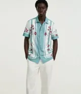 Pantalón de vestir blanco, de corte recto, con bolsillos laterales y traseros. Se ajusta a la cintura con cinturón de cuero marrón.