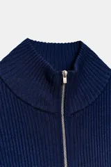 Chaqueta de punto acanalado azul marino con cuello alto y cierre frontal de cremallera metálica. Cuenta con detalles de rib en color blanco en los puños de las mangas largas.