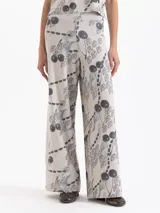 Pantalón de punto de tiro alto, pierna ancha y cintura elastizada. Presenta un estampado integral en tonos grises y negros sobre fondo beige claro, con motivos de cerezas, figuras estilizadas y cadenas.