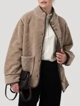 Chaqueta de polar color beige con diseño acolchado de rombos y ribetes en contraste. Presenta cierre frontal de botones, cuello alto, manga larga y bolsillos delanteros aplicados. Confeccionada en poliéster reciclado con detalles de cuero.