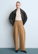 Pantalón tipo jeans de corte wide leg y tiro medio, confeccionado en denim de algodón color tostado. Presenta diseño de cinco bolsillos, cierre frontal con botón y cremallera, y costuras reforzadas.